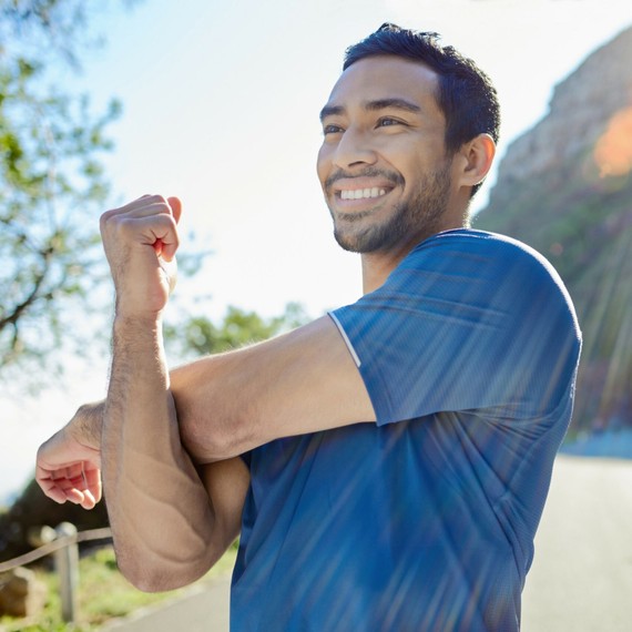a smiling man stretching his left arm doing exercise